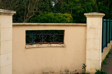 Beige stone wall with iron grill and greenery in daylight setting