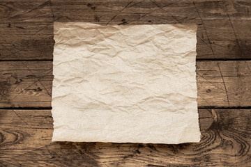 Old wrinkled paper sheet on rustic wooden table, vintage background texture for text, menu, design template, or rustic mockup
