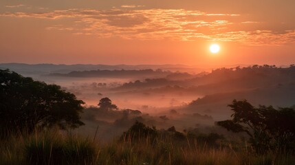 A scenic view of a sunrise over a misty landscape with trees and hills in the distance at golden hour