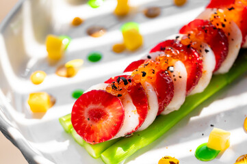 A stylish sushi roll featuring sliced strawberries and cream, garnished with fish roe and colorful sauces, elegantly presented on a decorative plate.