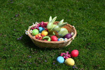 a sunlit easter basket with two easter bunnies and lots of colorful easter eggs on the green grass on a fine April day	