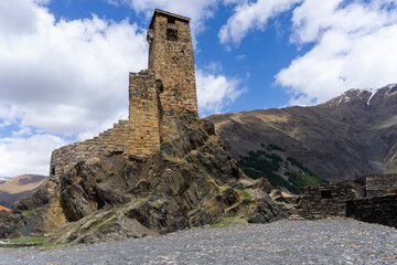 Fototapeta premium Fortress in the village of Sno on a cliff. Two stone towers with loopholes, a high defensive wall. Mountains, bright blue sky with clouds.