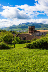 Romanesque cathedral of Saint-Lizier and its hexagonal brick bell tower with the green mountains of the Couserans in the background in spring