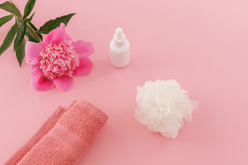 Towel with body care products and a peony flower on the pink background.