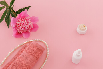 Towel with body care products and a peony flower on the pink background.