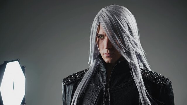 Sephiroth cosplayer wearing a black leather jacket and long silver wig posing in a studio with a softbox illuminating him during a photoshoot
