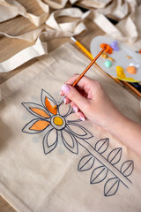 Woman's hand painting a flower on a canvas tote bag using acrylic paints. Close-up of a female hand painting a floral pattern on a reusable canvas bag with orange and yellow acrylic paints. Reuse © Светлана Мищенко