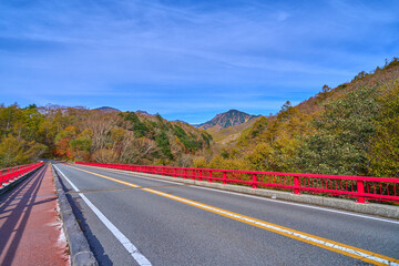 秋の山梨県北杜市の川俣川渓谷にかかる赤い橋(東沢大橋)と八ヶ岳