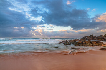 Sunrise at the seaside with rocks and rain clouds