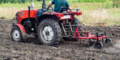 A farmer cultivates the field with a compact tractor preparing the soil for planting crops in the countryside. © Andrii_Abriutin