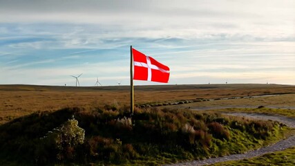 Danish flag fluttering over grassy plain with wind turbines under soft sky

 - Powered by Adobe