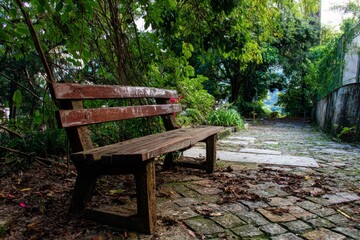 Fototapeta premium An old wooden bench sits in a peaceful park, with a path leading into the lush, green garden.