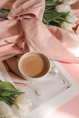 Flat lay with white tulips in a soft pink denim jacket, a fashion magazine, and a cup of coffee on a pastel pink background — cozy, stylish morning scene with feminine spring mood