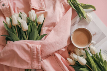 Flat lay with white tulips in a soft pink denim jacket, a fashion magazine, and a cup of coffee on a pastel pink background — cozy, stylish morning scene with feminine spring mood