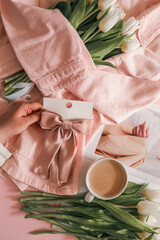 White tulips wrapped in a soft pink denim jacket with a satin pink hair bow on a card, styled on a...