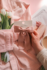 White tulips wrapped in a soft pink denim jacket with a satin pink hair bow on a card, styled on a...