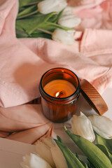 Burning candle, white tulips, and pink denim jacket on soft surface — aesthetic flatlay with gentle light, cozy spring mood, and feminine composition
