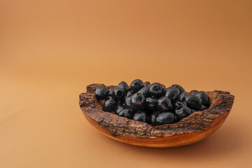 Rustic wooden bowl filled with shiny black olives on warm brown background. Organic healthy snack in natural serving dish. Minimalist food presentation with earthy tones
