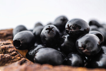 Rustic wooden bowl filled with glossy black olives placed on a clean white background. Minimalist food concept with natural textures and healthy organic snack