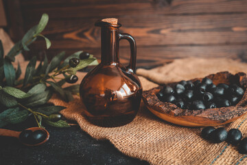 Rustic still life composition with black olives in a wooden bowl, a wooden spoon, olive branch, and...