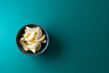 Colorful banana-shaped gummy candy in bowl on vibrant green background with copy space for sweet snack concept