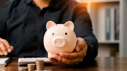 Concepts of saving money and financial planning. Man hand holding piggy bank on wood table, income, return, retirement, compensation fund, investment, dividend tax, stock market