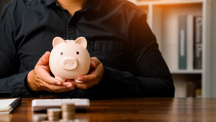 Concepts of saving money and financial planning. Man hand holding piggy bank on wood table, income, return, retirement, compensation fund, investment, dividend tax, stock market