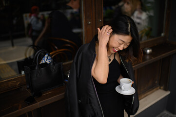 Asian woman standing alone by a café bar counter on a city street, enjoying her morning coffee and quietly observing the urban scenery before starting her workday.