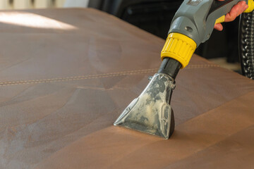 Cleaning a brown sofa with a washing vacuum cleaner. Spring Cleaning in the Apartment