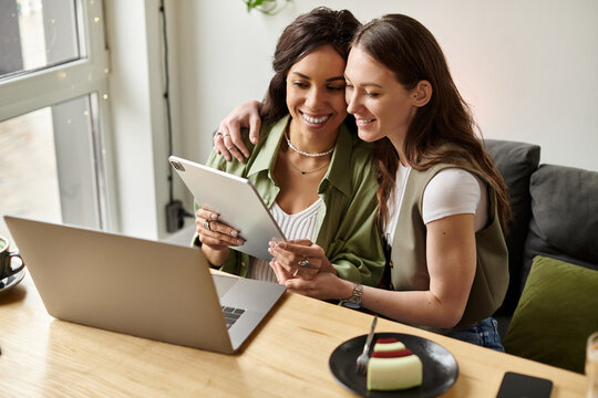 Happy lesbian couple enjoying a cozy moment at a cafe while using a tablet and sharing smiles