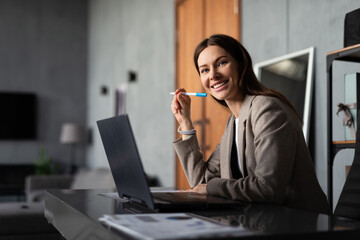 Professional woman working in office. She is seated at desk with a laptop and documents.