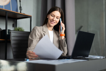 Business female talking on phone at desk and holding a document.