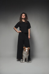 Young beautiful woman with curly hair and in black clothes with a border collie puppy. The dog obediently sits at her feet.