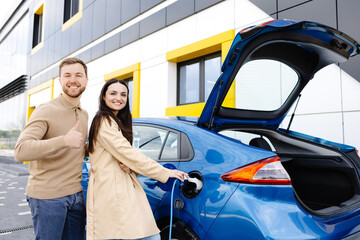 Young couple man and woman traveling by electric car having stop at charging station. Girlfriend...