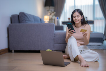 Young woman sitting on the floor at home is shopping online using laptop, smartphone and credit card, enjoying online shopping and cashless payment © Tj