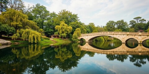 Fototapeta premium Arch Bridge Over Tranquil Waters: A picturesque arch bridge gracefully spans a serene river, its reflection mirroring the lush greenery and the expansive sky above.