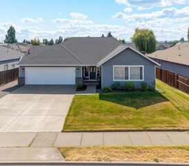 Fototapeta premium Front view of a modern home with a gray exterior, double garage, and manicured lawn. The home features a gray shingle roof, light gray siding, and a light colored driveway