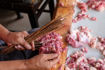 The goat satay seller is skewering slices of goat meat onto the skewers. mutton satay. sate kambing. blurred image. 