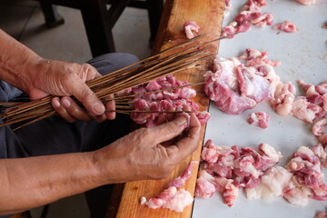 The goat satay seller is skewering slices of goat meat onto the skewers. mutton satay. sate kambing. blurred image. 