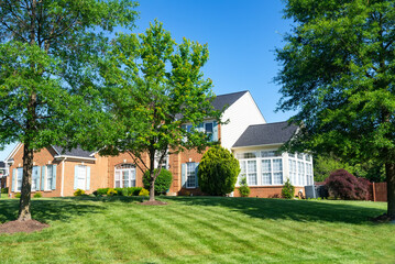 Obraz premium Big luxury house with nicely landscaped front yard and mowed lawn in the suburbs. Summer day, blue sky.