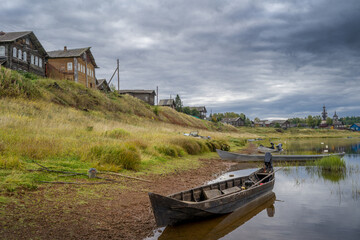 Boats on the river bank against the backdrop of log houses and an old wooden church.