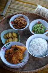 Indonesian cuisine served on a bamboo tray. rice, stir-fried chayote, stir-fried tempeh, balado chicken, fried tofu, crackers. Tumis labu siam, ore tempe, Tahu goreng, ayam bumbu pedas.
