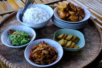 Indonesian cuisine served on a bamboo tray. rice, stir-fried chayote, stir-fried tempeh, balado chicken, fried tofu, crackers. Tumis labu siam, ore tempe, Tahu goreng, ayam bumbu pedas.