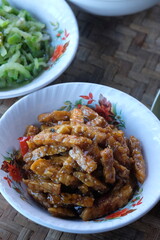 orek tempe or oseng tempe. made from tempeh, sliced garlic, shallots, chili, soy sauce. Indonesian food. served in a white bowl