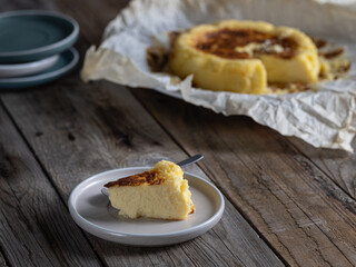 Close-up of a slice of La Viña cheesecake with freshly baked cake in the background. Homemade pastries in a rustic setting.