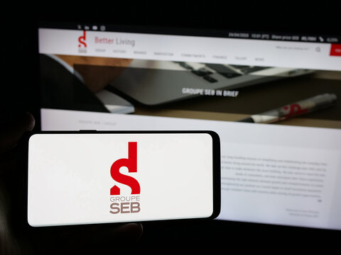 Stuttgart, Germany - 04-25-2025: Person holding smartphone with logo of French appliances company SEB S.A. on screen in front of website. Focus on phone display.