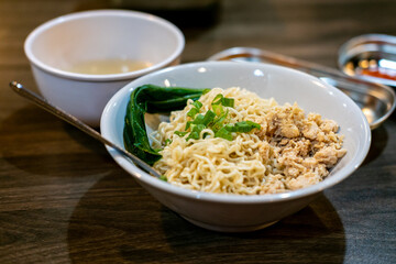 A bowl of Mie Ayam (chicken noodles) with seasoned chicken, bok choy, and scallions, accompanied by broth and chili sauce. Popular Indonesian comfort food.