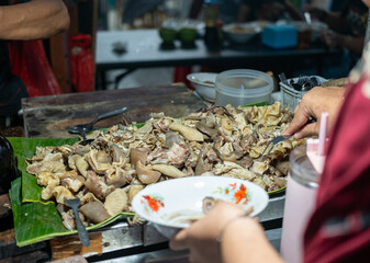 A street food vendor prepares Sop Kambing (mutton soup), with various cuts of lamb on banana leaves, serving into a white bowl. Authentic and bustling.