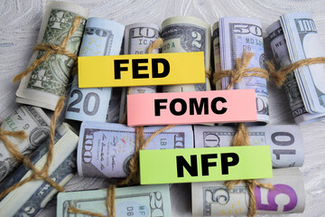 Concept of FED - FOMC - NFP write on sticky notes with dollars isolated on Wooden Table.