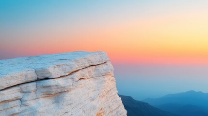 A rocky cliff edge overlooks distant mountains beneath a colorful sunrise or sunset sky.